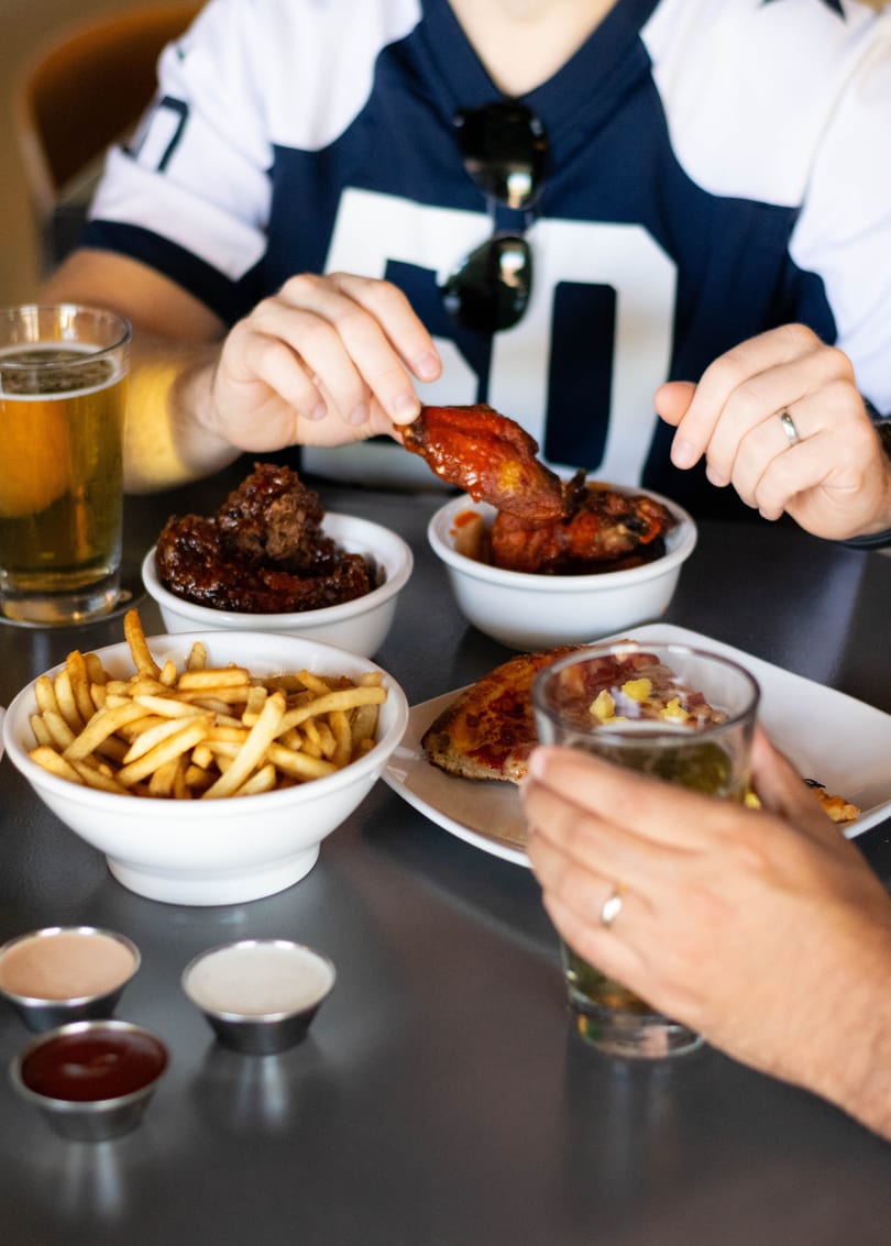 Two people enjoying chicken wings, fries, and beer at a table with various dipping sauces.