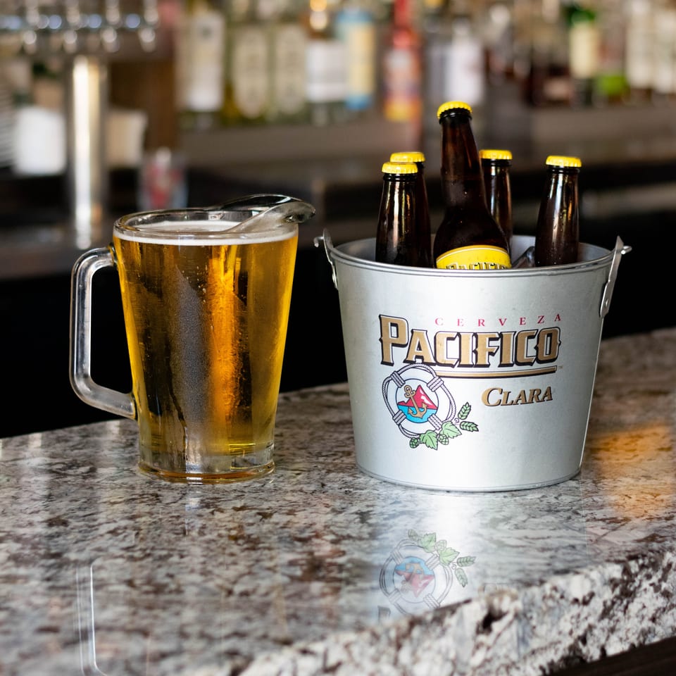 A pitcher of beer and a bucket of Pacifico Clara bottles sit on a granite bar top.