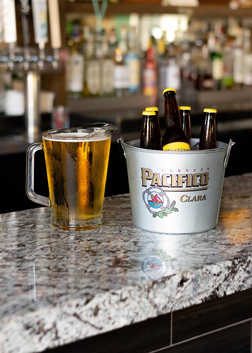 A pitcher of beer and a bucket of Pacifico Clara bottles sit on a granite bar top.