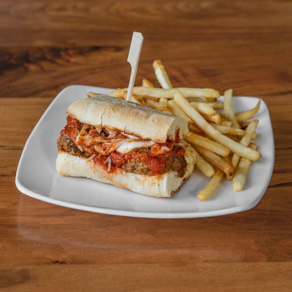 Meatball sub with melted cheese and red sauce, served with a side of french fries.