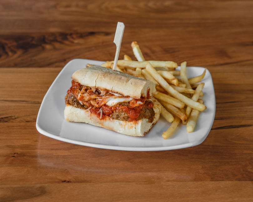 Meatball sub with melted cheese and red sauce, served with a side of french fries.