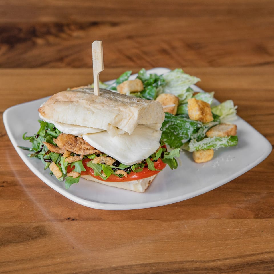 A sandwich with mozzarella, tomatoes, arugula, and crispy onions, served with a side salad.