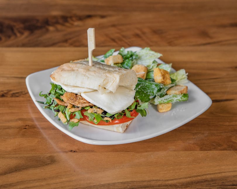 A sandwich with mozzarella, tomatoes, arugula, and crispy onions, served with a side salad.