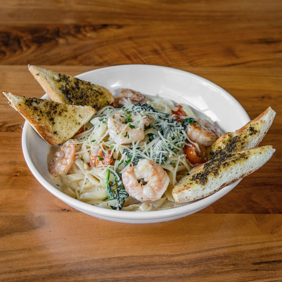 Creamy shrimp pasta with spinach, tomatoes, and parmesan cheese, served with garlic bread on a wooden table.
