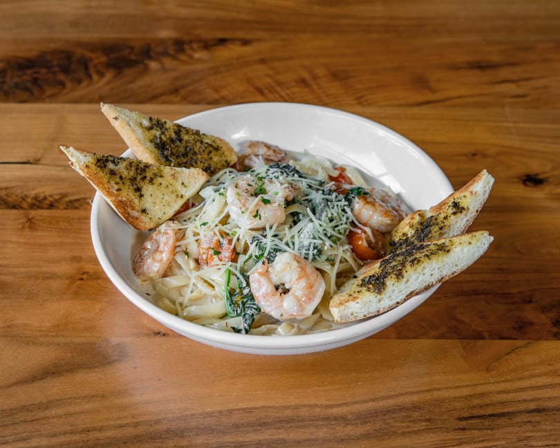 Creamy shrimp pasta with spinach, tomatoes, and parmesan cheese, served with garlic bread on a wooden table.