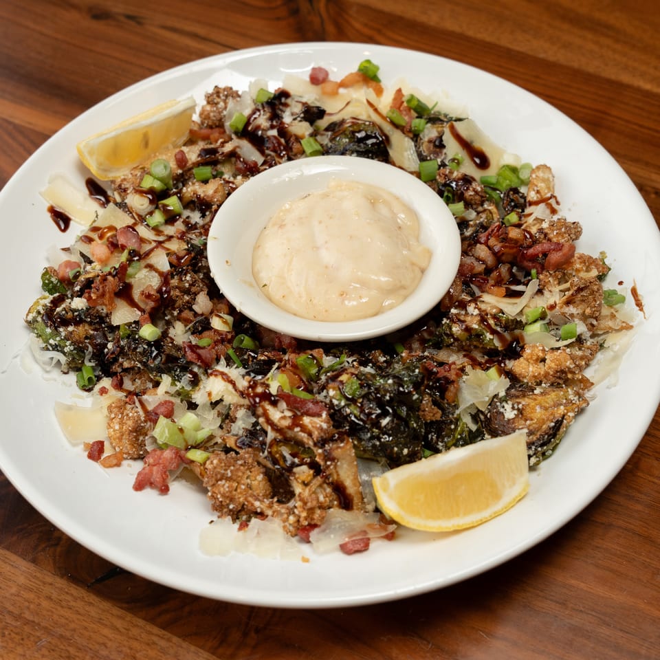 Crispy Brussels sprouts and cauliflower with bacon, cheese, balsamic glaze, and a side of dipping sauce.