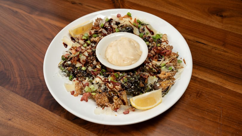 Crispy Brussels sprouts and cauliflower with bacon, cheese, balsamic glaze, and a side of dipping sauce.